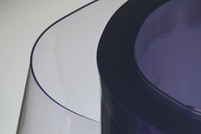 Un grand rouleau de vinyle PVC semi-transparent avec une légère teinte bleutée, partiellement déroulé pour révéler son matériau lisse et flexible.