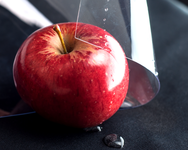 Una lámina brillante y transparente de vinilo de PVC que cubre parcialmente una manzana roja con gotas de agua en su superficie, lo que demuestra sus propiedades alimentarias.