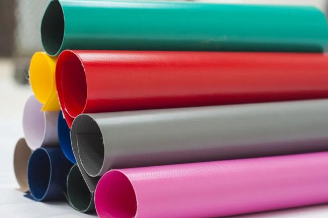 rolled sheets of colorful PVC coated fabrics in various shades including green, red, yellow, grey, and pink, used for industrial tarpaulins and curtains  Image 2 (gym divider curtains): large indoor gymnasium with retractable blue and white vinyl divider curtains hanging from the ceiling to separate sports courts  Image 3 (industrial yellow partition): industrial warehouse space with yellow vinyl curtain walls and clear PVC viewing panels used for sectioning off work areas  Let me know if you'd like alt tex